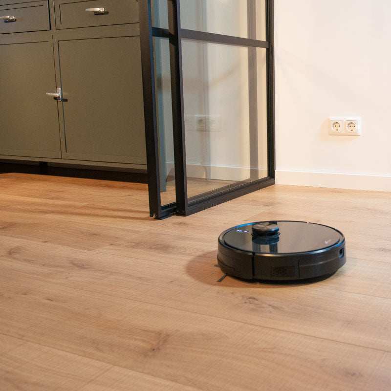 Beste robotstofstuiger met dweilfunctie Willem met leegstation op houten vloer bij glazen deur